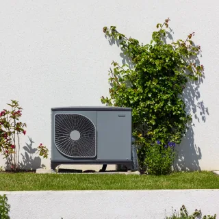 Buitenunit van een warmtepomp tegen de gevel van een woning
